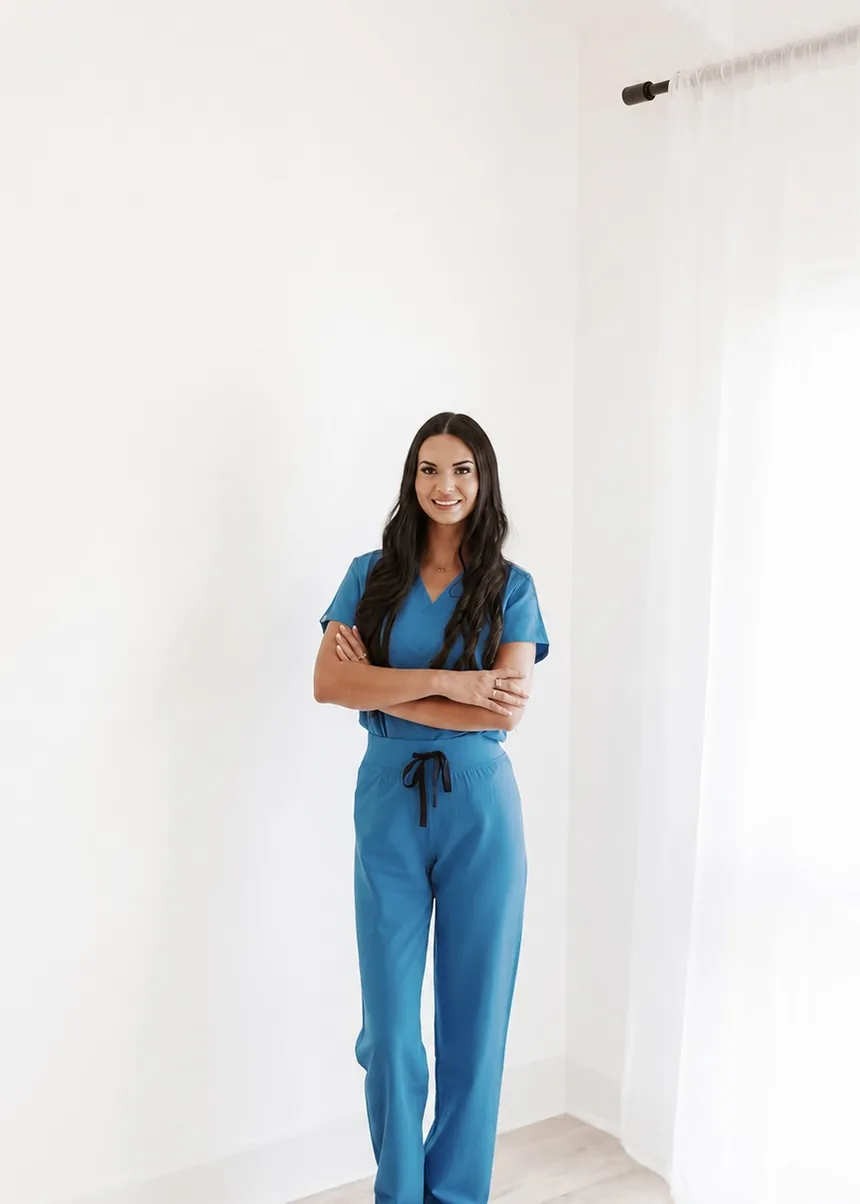 A woman in blue scrubs standing in a bright white room